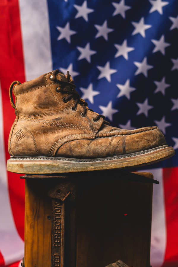 Brown leather boot on a wooden block with an American flag in the background