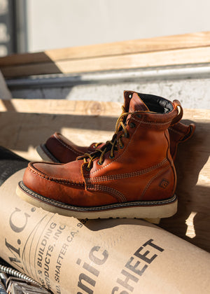 Brown leather boots on a wooden surface with a cardboard box underneath