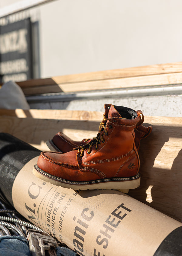 Brown leather boots on a wooden surface with a cardboard box underneath