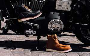 Brown leather boots next to a motorcycle with a visible Harley-Davidson logo.