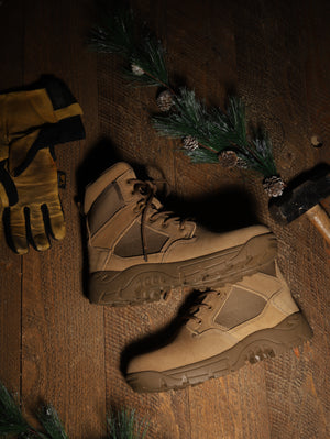 Pair of tactical boots and gloves on a wooden surface with pine branches.