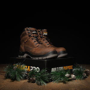 Brown work boot on a black box with 'Danner' branding, surrounded by greenery on a dark background.
